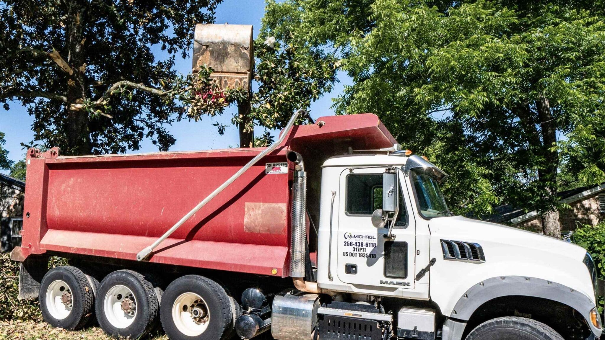 McMichael Waste Services Mack dump truck with an excavator bucket raised above its bed during demolition debris haul-off in Alabama