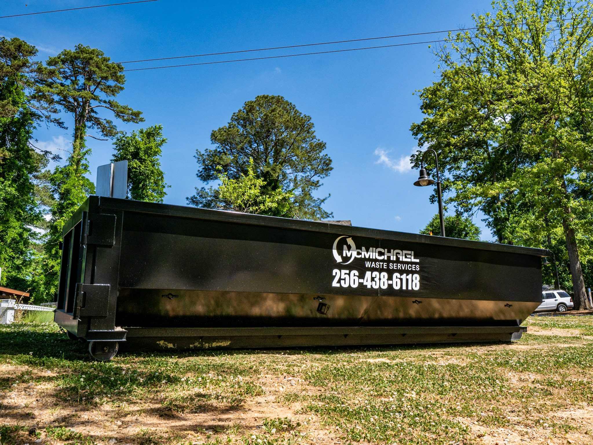 McMichael Waste Services branded black roll-off container set on grass under trees in Alabama