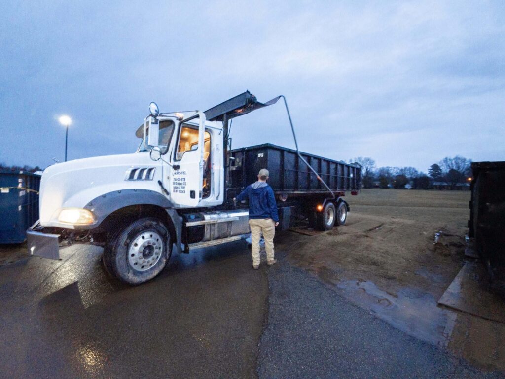 McMichael Waste Services roll-off truck with the hoist raised and a container on the rails at blue hour in Alabama