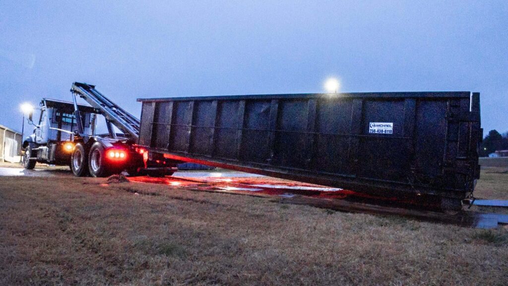 McMichael Waste Services roll-off truck setting a branded container down on mats at dusk in Alabama