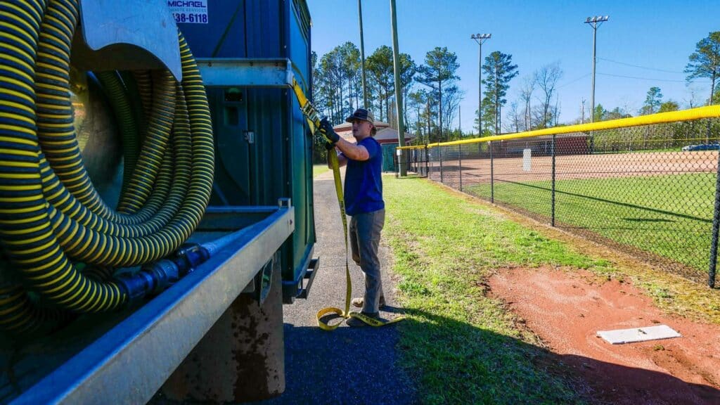 McMichael Waste Services crew member working at the vacuum truck beside a ball field