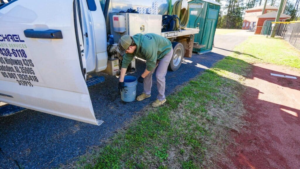 McMichael Waste Services vacuum truck with its US DOT number 1935418 and Gadsden, Alabama address on the open driver's door, a crew member lifting a bucket alongside