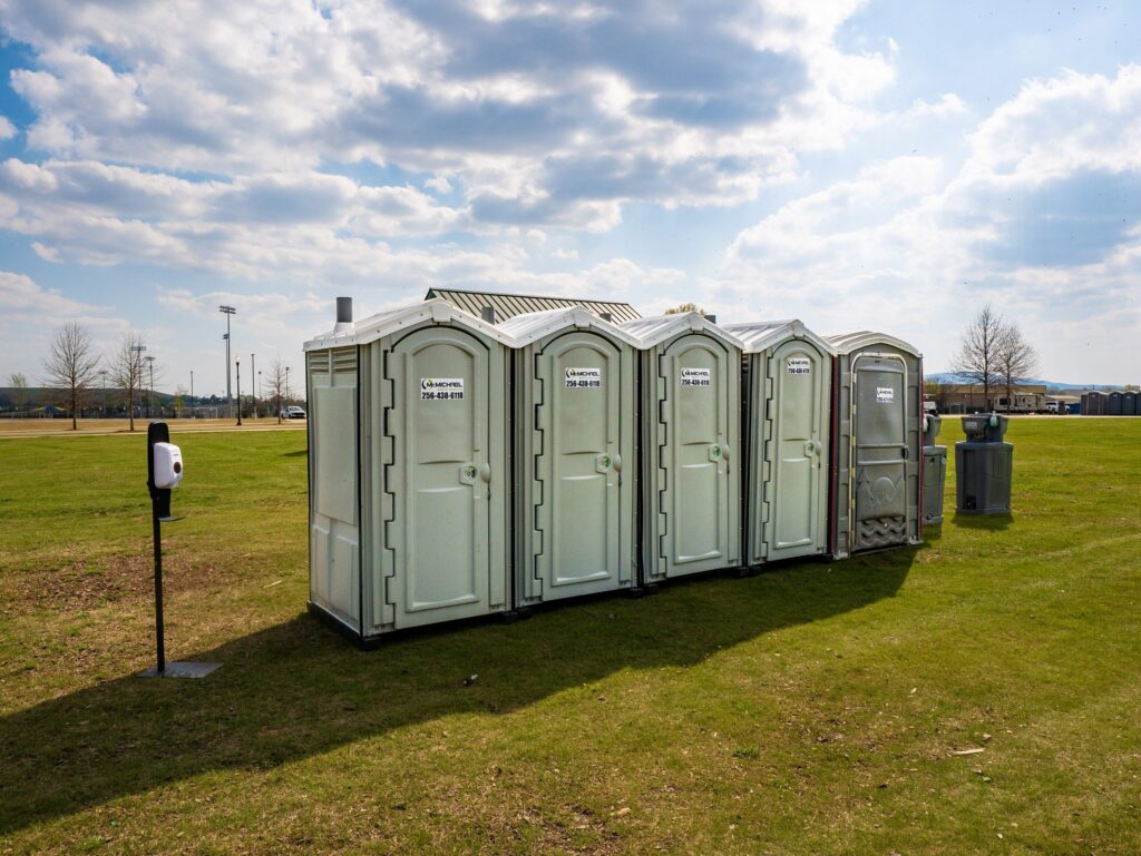McMichael Waste Services portable toilets and a hand-sanitizer stand set up on an open field