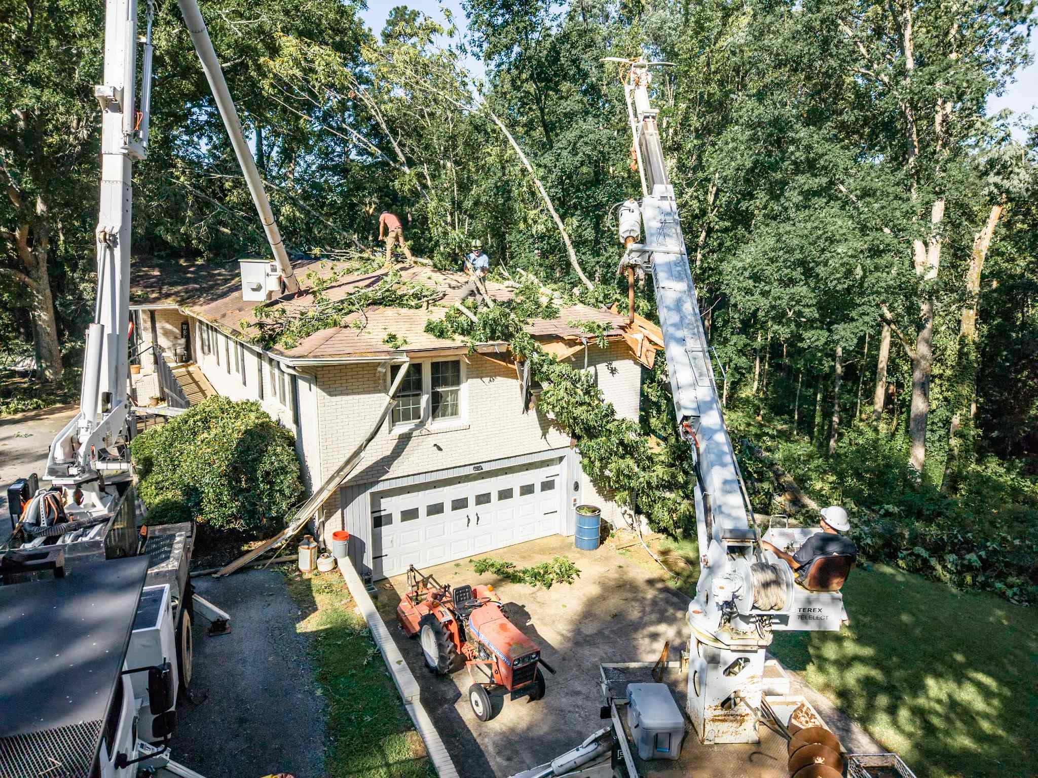 Crane lifting a fallen tree off a home's garage during storm cleanup in Alabama