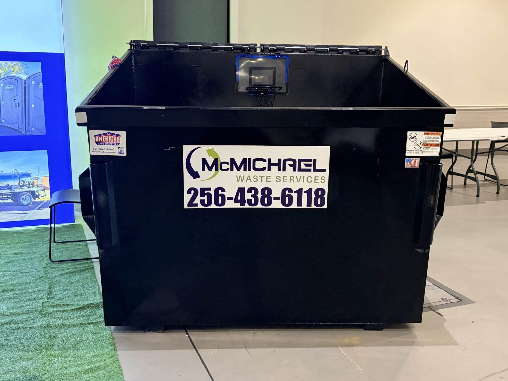 Black McMichael Waste Services commercial front-load dumpster with the 256-438-6118 phone number on the front