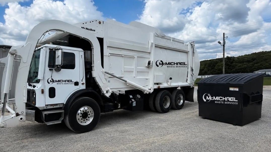 McMichael Waste Services front-load garbage truck parked beside a black commercial front-load dumpster in Alabama