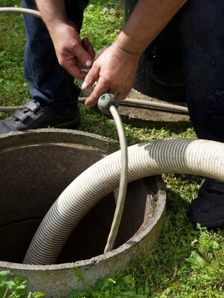Technician lowering a vacuum hose into an in-ground tank riser in Alabama