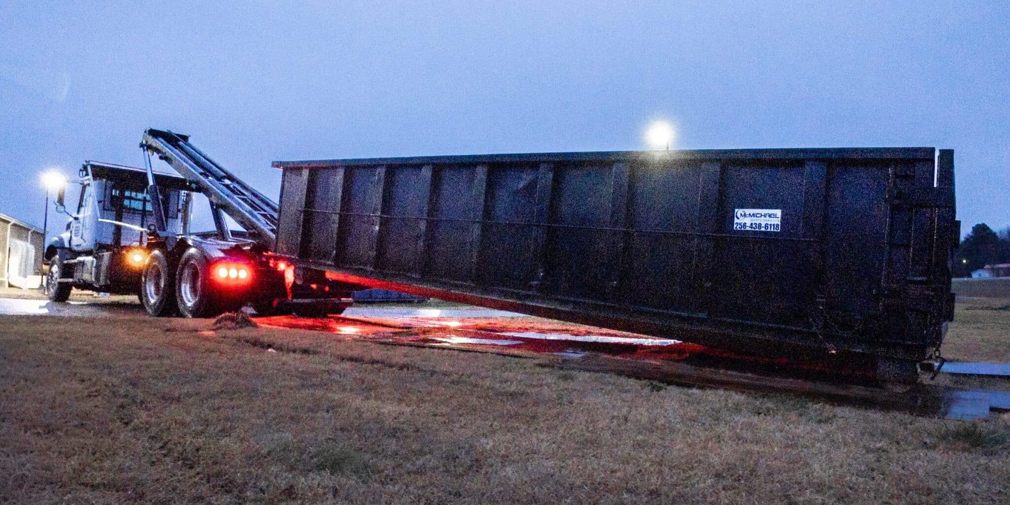 McMichael Waste Services roll-off truck setting a container at dusk