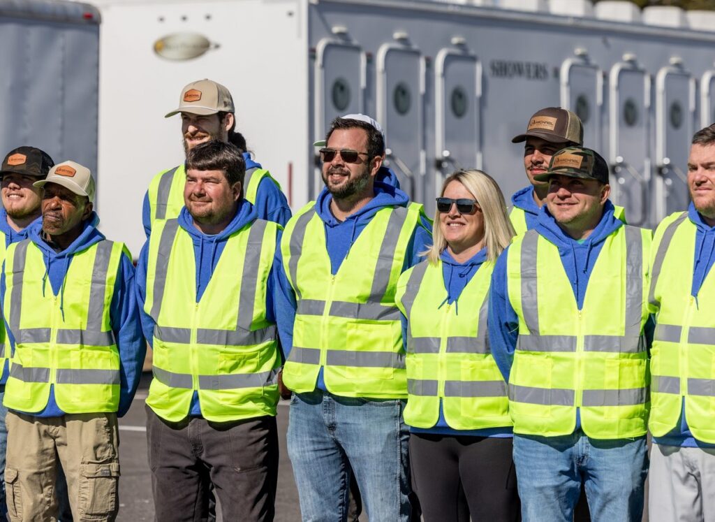 McMichael Waste Services crew in safety vests standing in front of a shower trailer