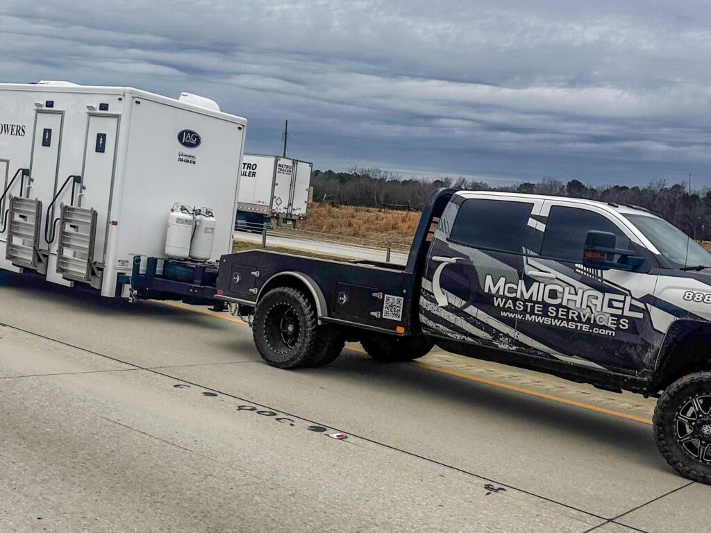 McMichael Waste Services branded truck hauling a restroom and shower trailer on the highway
