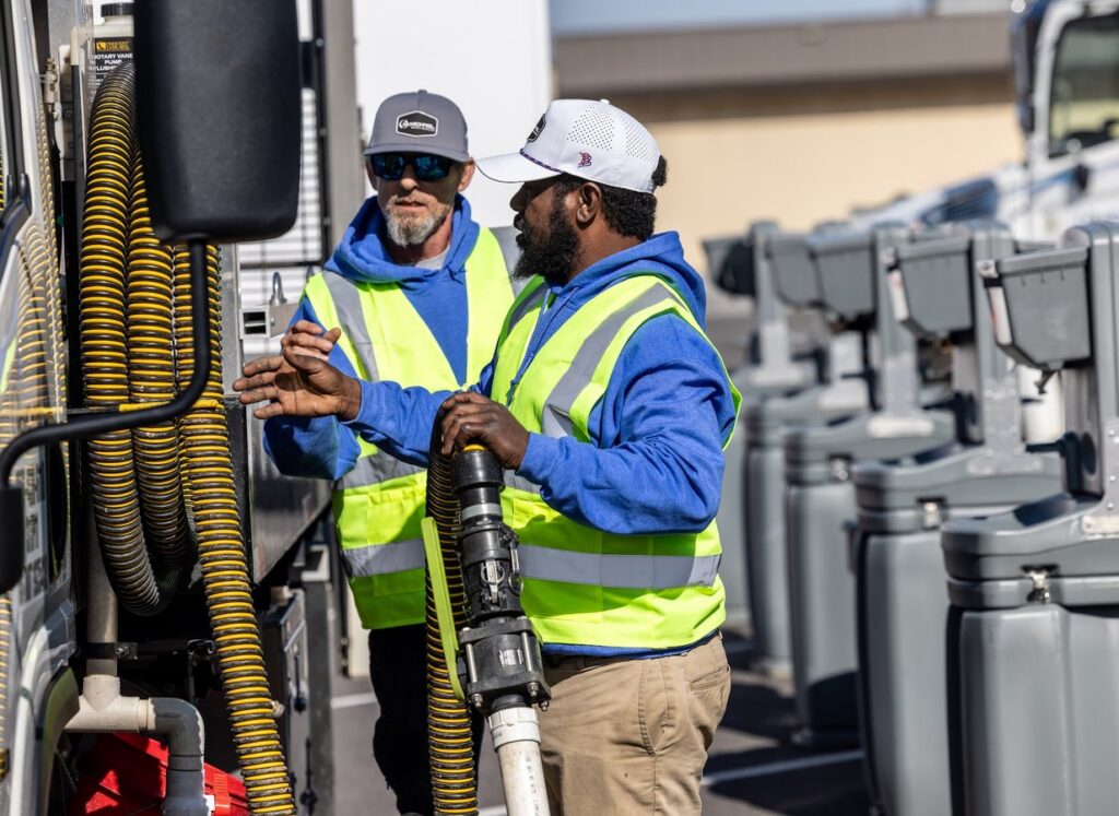 McMichael Waste Services crew members in safety vests servicing portable sanitation units with a vacuum hose